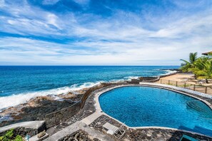 A pool with a curved edge, surrounded by a stone deck and a railing, overlooking the ocean. - Great Location - Close to Ocean - Central AC - Vrkcv (Kailua-Kona)