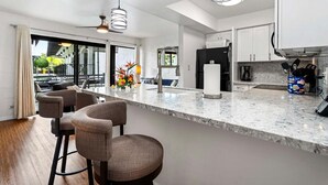 A modern kitchen with a marble countertop, bar stools, and a refrigerator. - Great Location - Close to Ocean - Central AC - Vrkcv (Kailua-Kona)