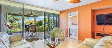 A spacious living area with a glass wall, a ceiling fan, a TV, and a dining area with outdoor views.