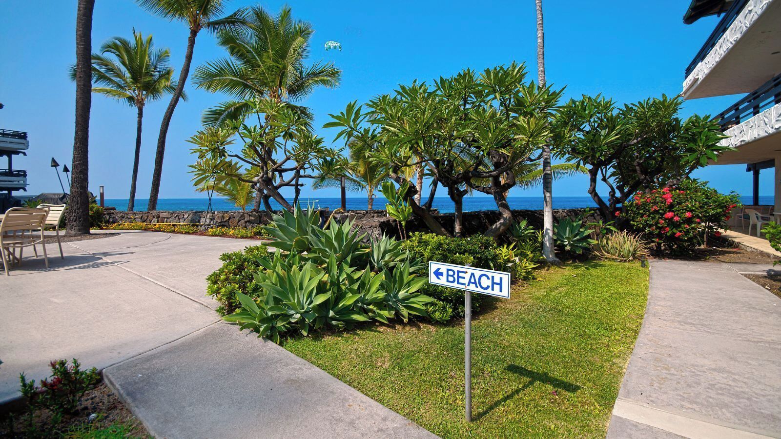 A beachfront hotel with a sign indicating the direction to the beach, palm trees, and a clear view of the ocean.