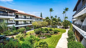 A hotel courtyard with multiple balconies, palm trees, and a well-maintained garden. - Complete Renovation - 20 Steps to Ocean -washer/dryer in Unit- Vrkcv (Kailua-Kona)