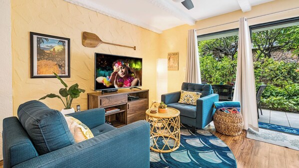 A living room with a sofa, armchair, TV, and a small round table. - Complete Renovation - 20 Steps to Ocean -washer/dryer in Unit- Vrkcv (Kailua-Kona)