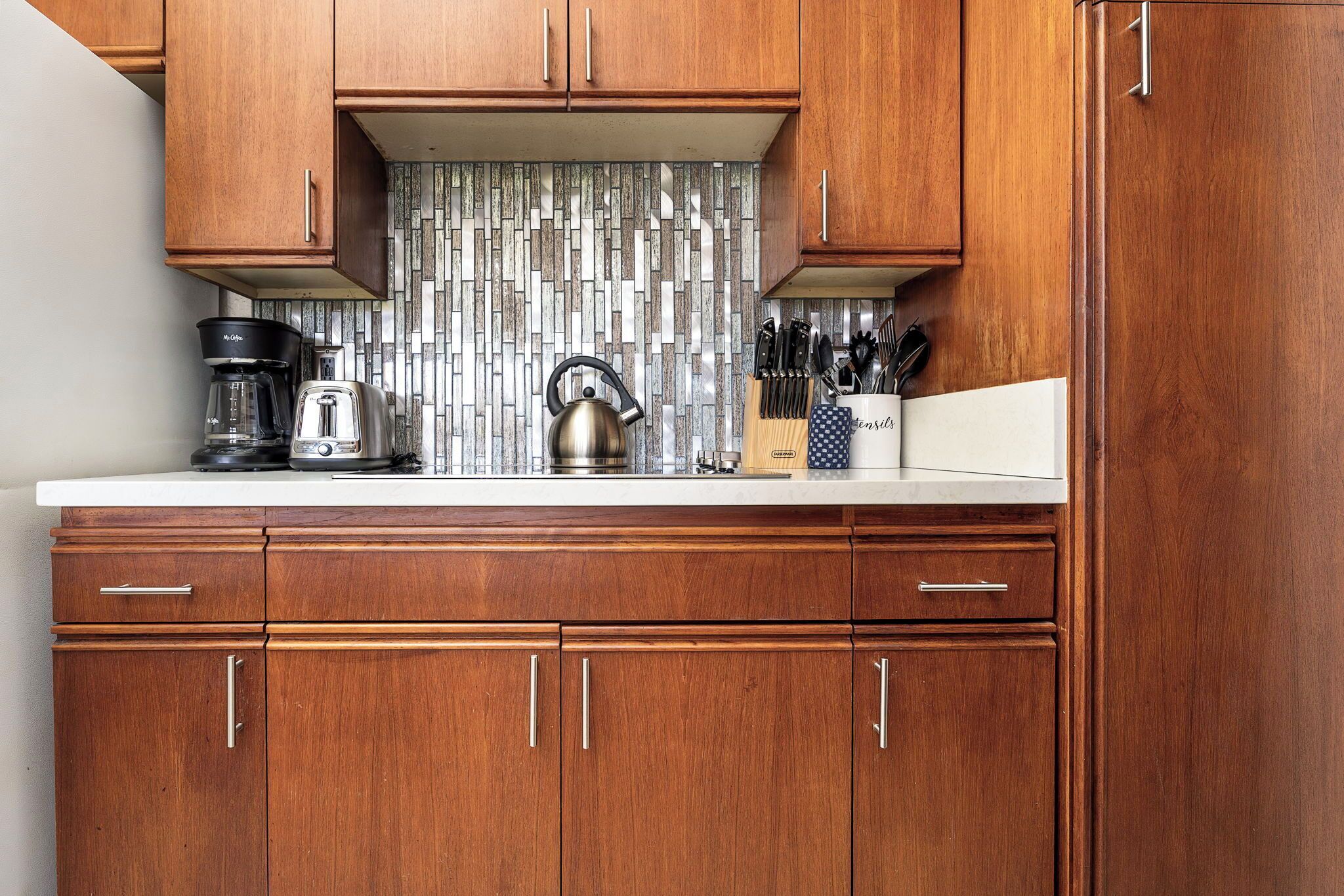 Una cocina con armarios de madera, una cafetera, un hervidor y un juego de cuchillos.