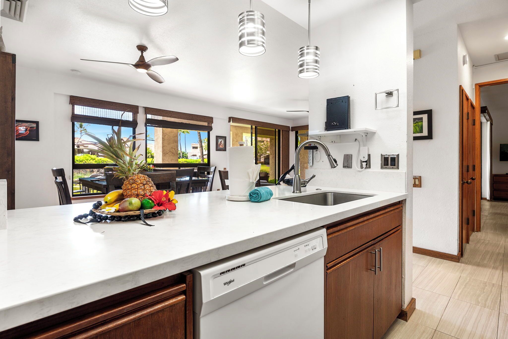 Una cocina moderna con encimeras blancas, armarios de madera, lavavajillas y una zona de comedor con mesa y sillas.