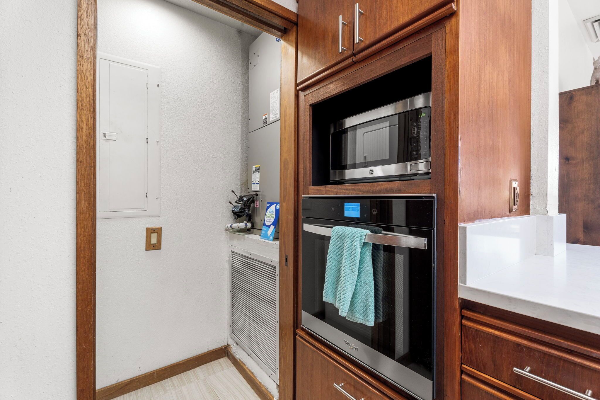 Une cuisine avec des meubles en bois, un four à micro-ondes, un four traditionnel et un plan de travail blanc.