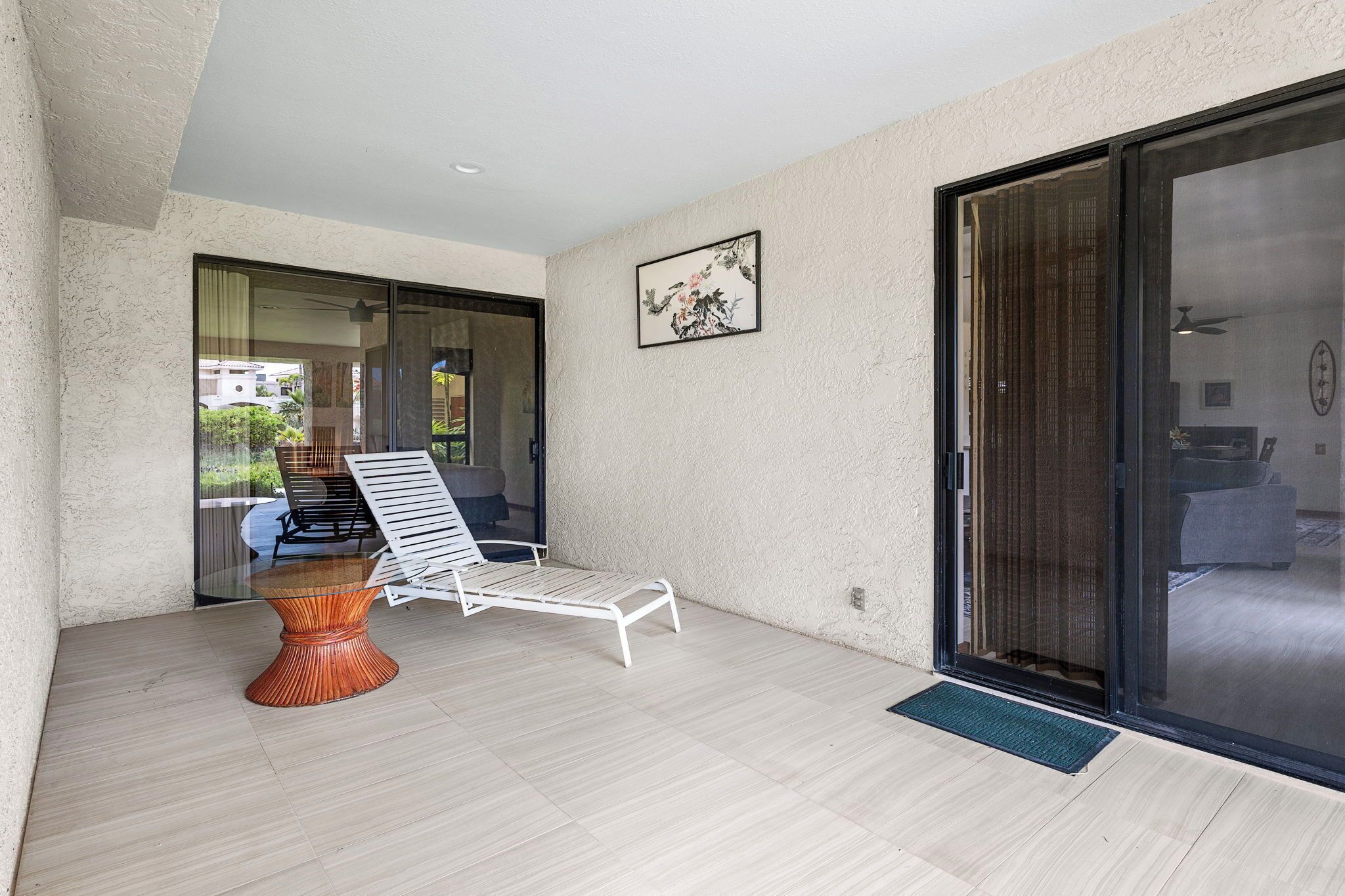 Une terrasse extérieure moderne avec une table en verre et des chaises blanches, une petite table d’appoint en bois et une porte-fenêtre coulissante donnant sur un balcon.