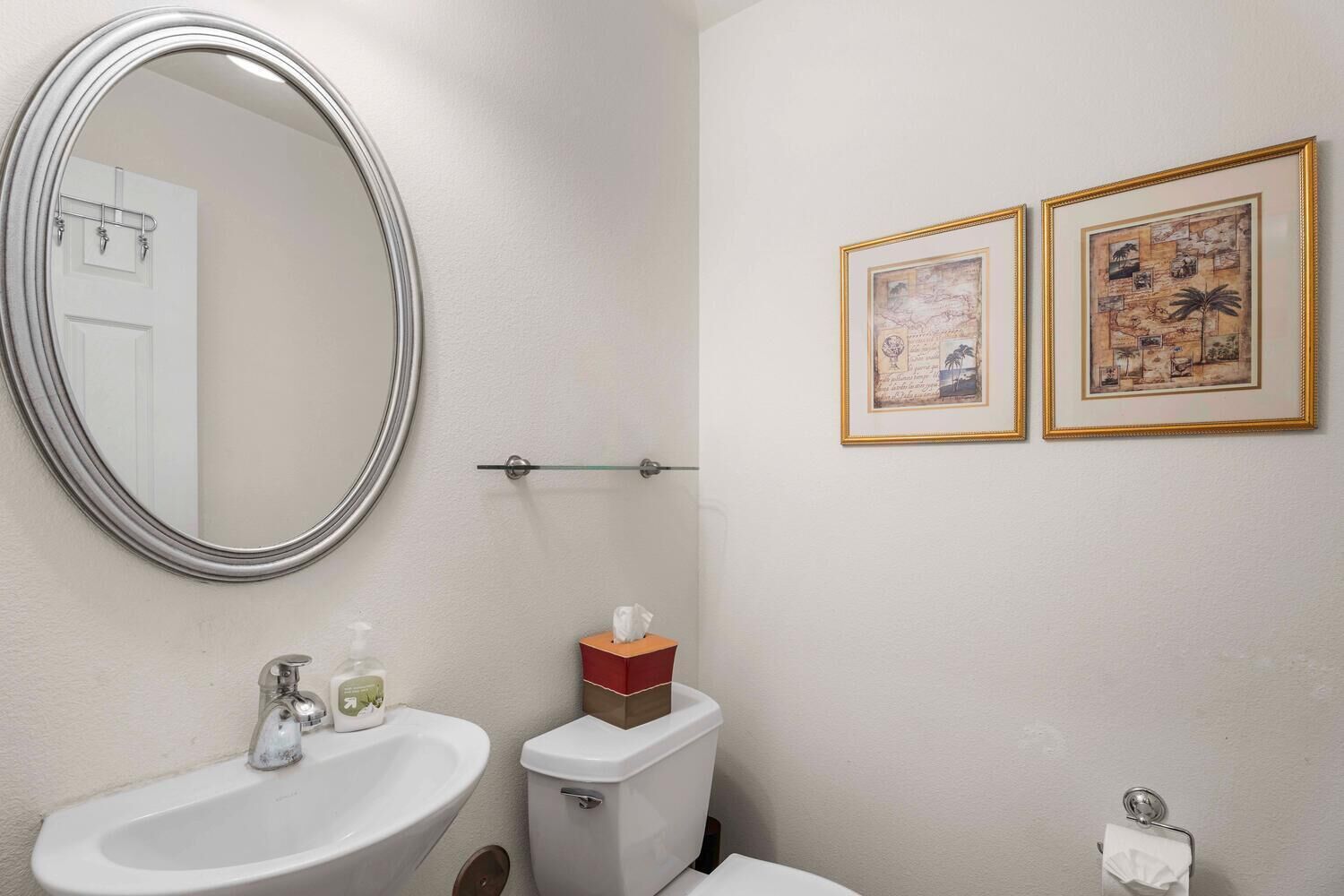 Un bagno con uno specchio tondo, un lavandino, un WC e due quadri appesi al muro.
