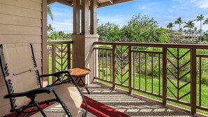 Un espacio al aire libre techado con una terraza de madera, un tapete rojo y vistas a un jardín ajardinado con palmeras.