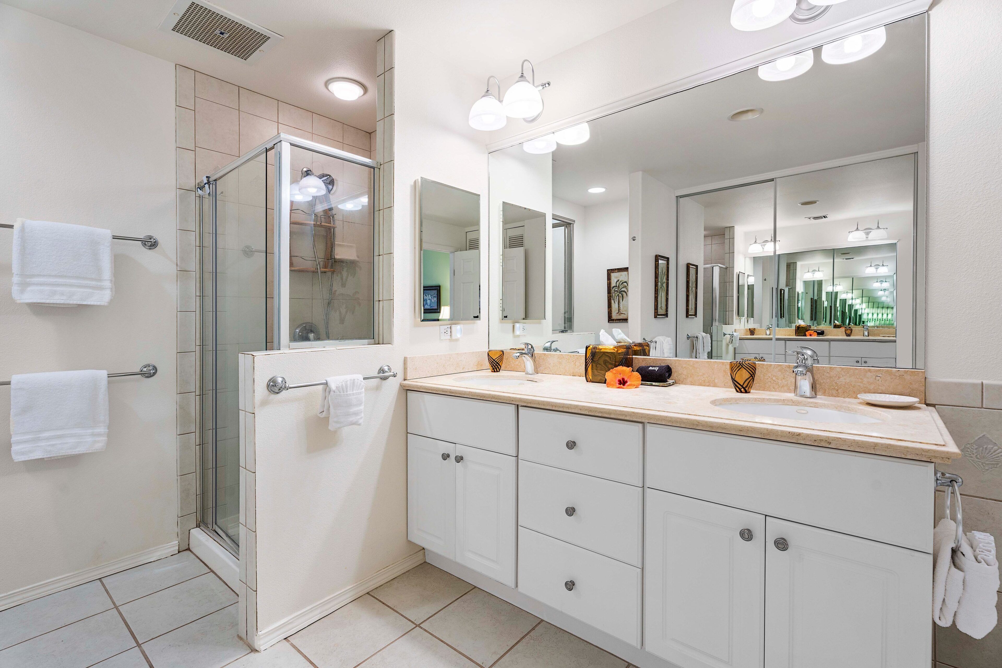 A modern bathroom with a glass shower enclosure, a large mirror, and a vanity with a sink and countertop.