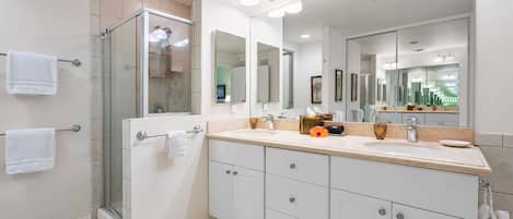 A modern bathroom with a glass shower enclosure, a large mirror, and a vanity with a sink and countertop.