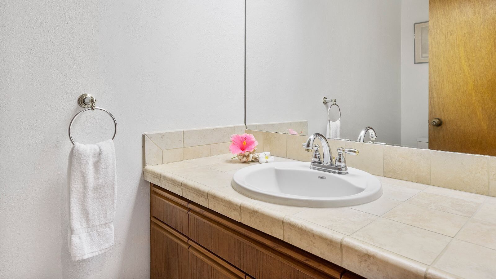 A bathroom with a white sink, wooden cabinets, a towel ring, and a mirror.