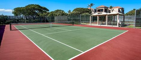 Una cancha de tenis con red, rodeada por una valla y árboles.