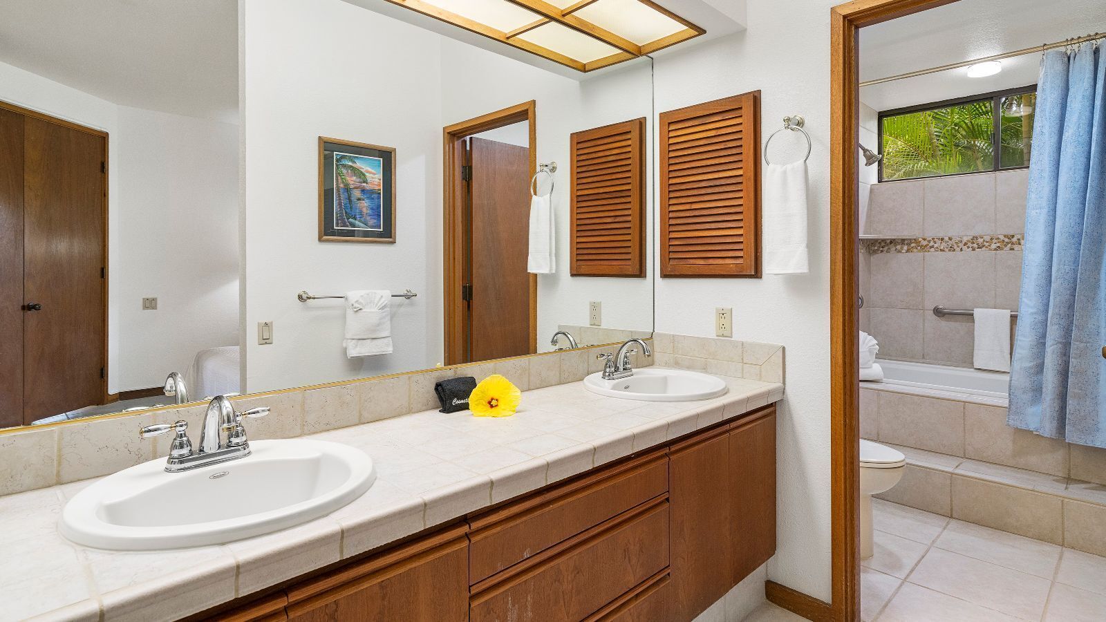 Un baño con dos lavamanos, armarios de madera, un espejo grande y una zona de ducha con cortina azul.