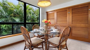 A dining area with a round glass table, wicker chairs, and a vase with flowers.
