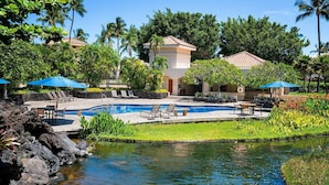 A resort pool area with lounge chairs, a small pool, and a building with a tiled roof.