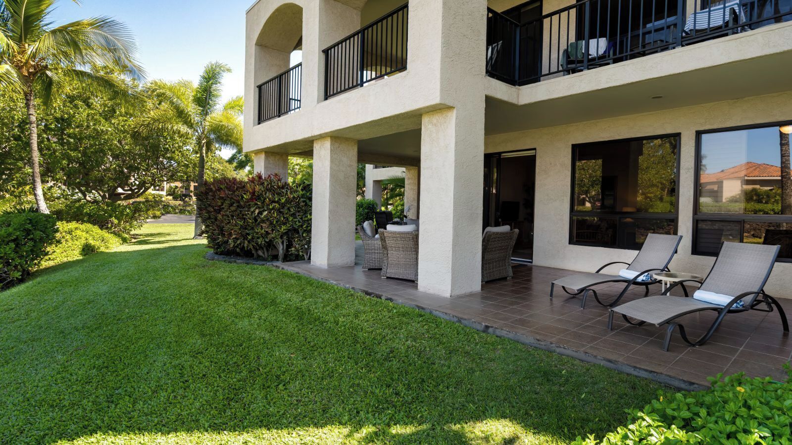 A modern two-story building with a balcony, outdoor seating area, and a well-maintained lawn.