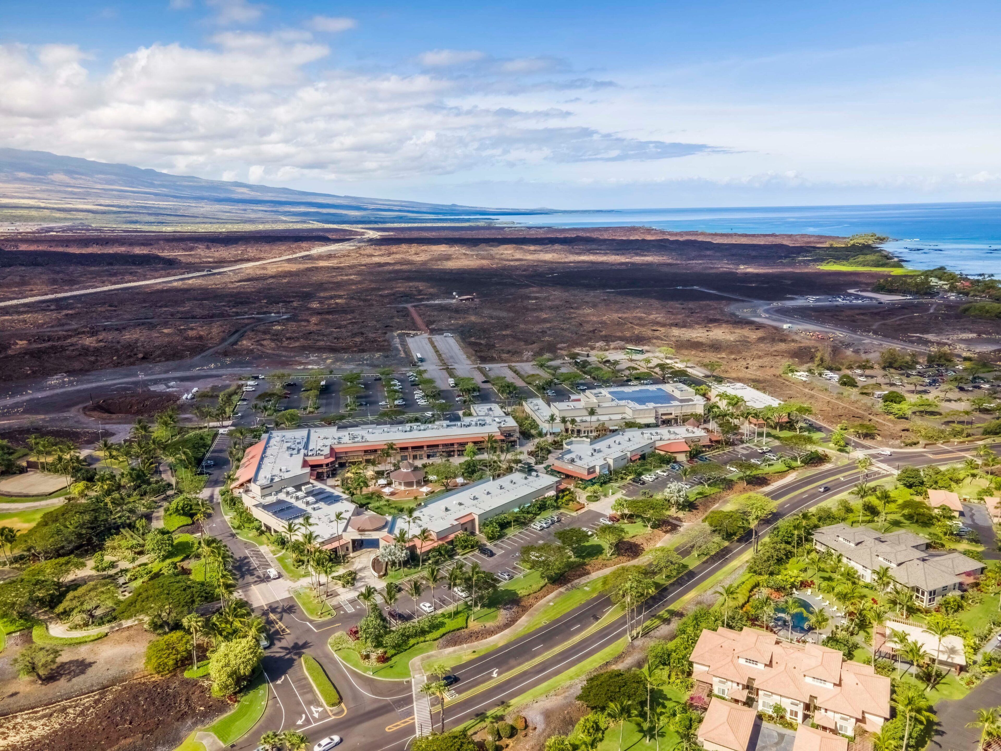 An aerial view of a coastal resort with multiple buildings, parking areas, and lush greenery.