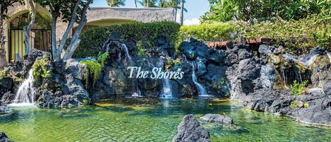 A tropical garden with a clear pond, waterfalls, and a stone bridge.