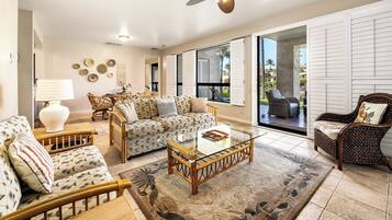 A spacious living room with a glass coffee table, wicker furniture, and a view of the outdoors.