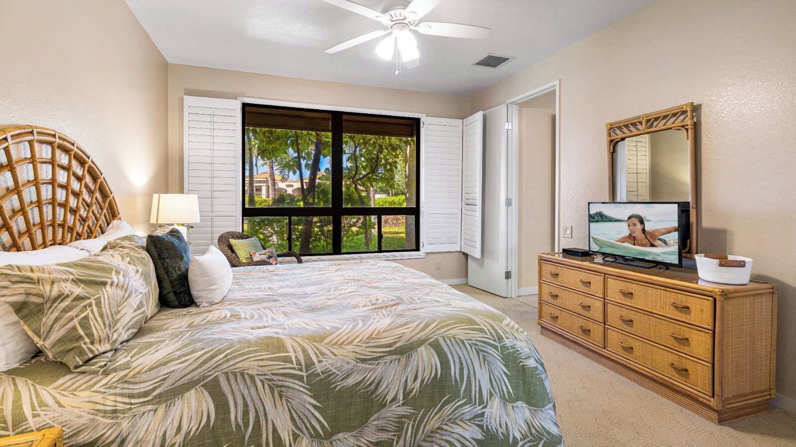 A bedroom with a bed, a television on a dresser, and a window with shutters.