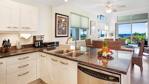 A modern kitchen with white cabinets, stainless steel appliances, and a large island with a fruit bowl. - Ocean View - AC & Wifi - Walk to Beach & Shopping - Vrkcv (Kailua-Kona)