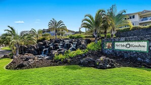 A sign for 'Na Hale Kauhou' with a rocky waterfall and palm trees in the foreground. - Ocean View - AC & Wifi - Walk to Beach & Shopping - Vrkcv (Kailua-Kona)