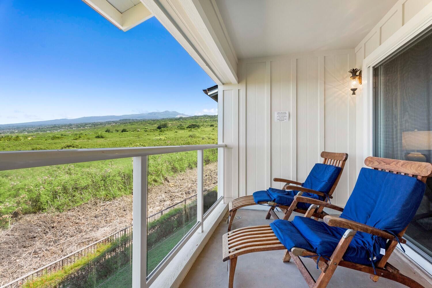 En balkon med to trægyngestole og gelænder af glas, der ud til et grønt landskab.