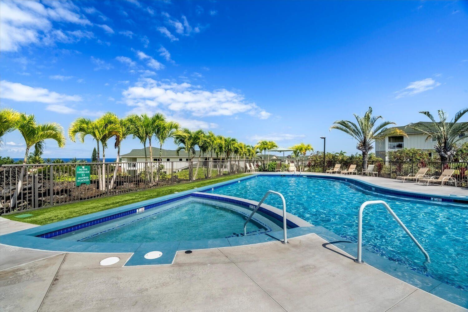 A swimming pool with a clear blue sky, palm trees, and a sign indicating no one under age allowed in Jacuzzis.