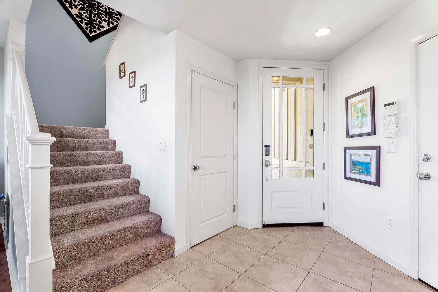 Un pasillo limpio y bien iluminado con una escalera alfombrada, paredes blancas y una puerta que da a otra habitación.