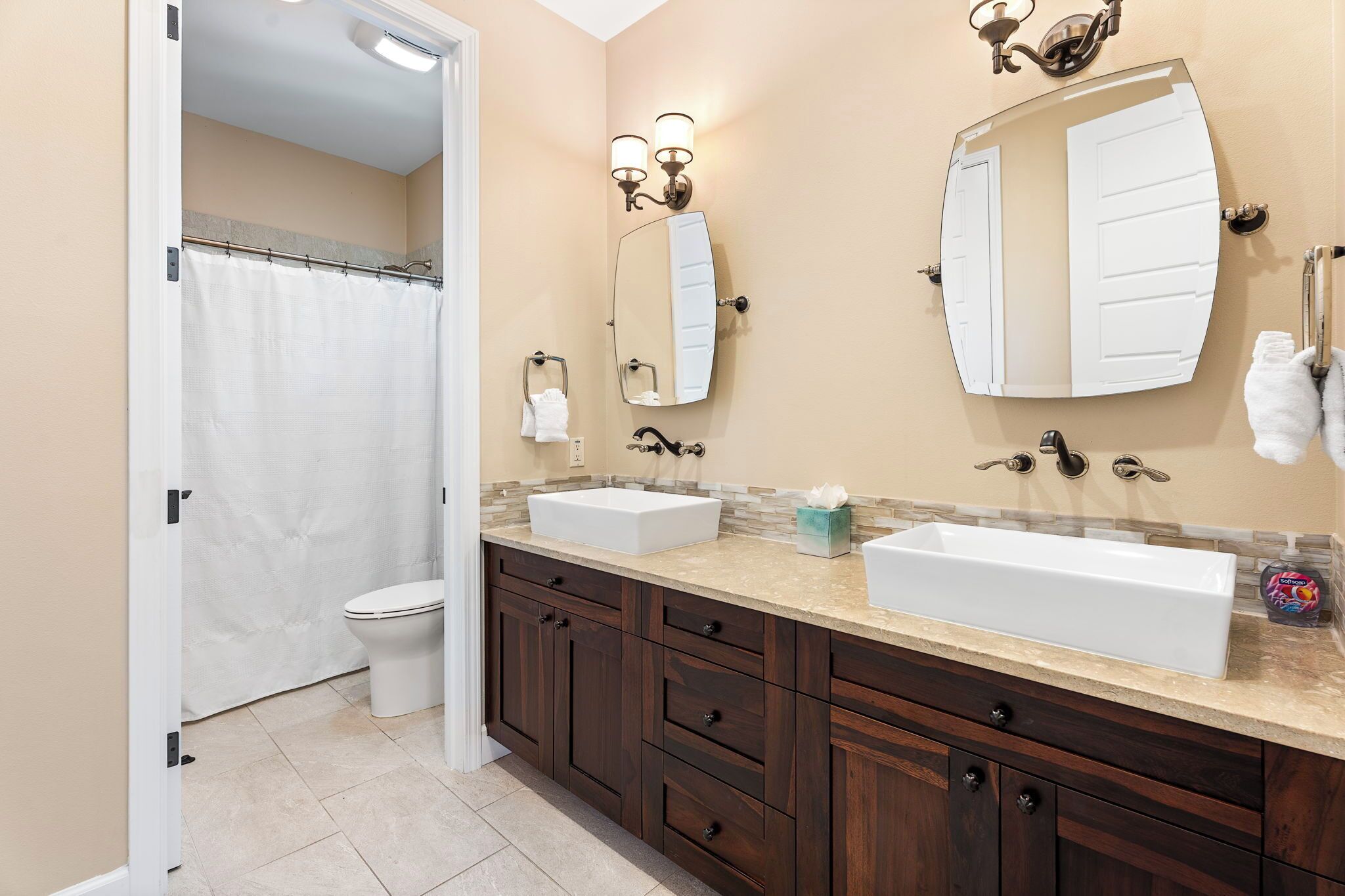A bathroom with a white toilet, a shower curtain, two sinks with vanity mirrors, and a towel rack.