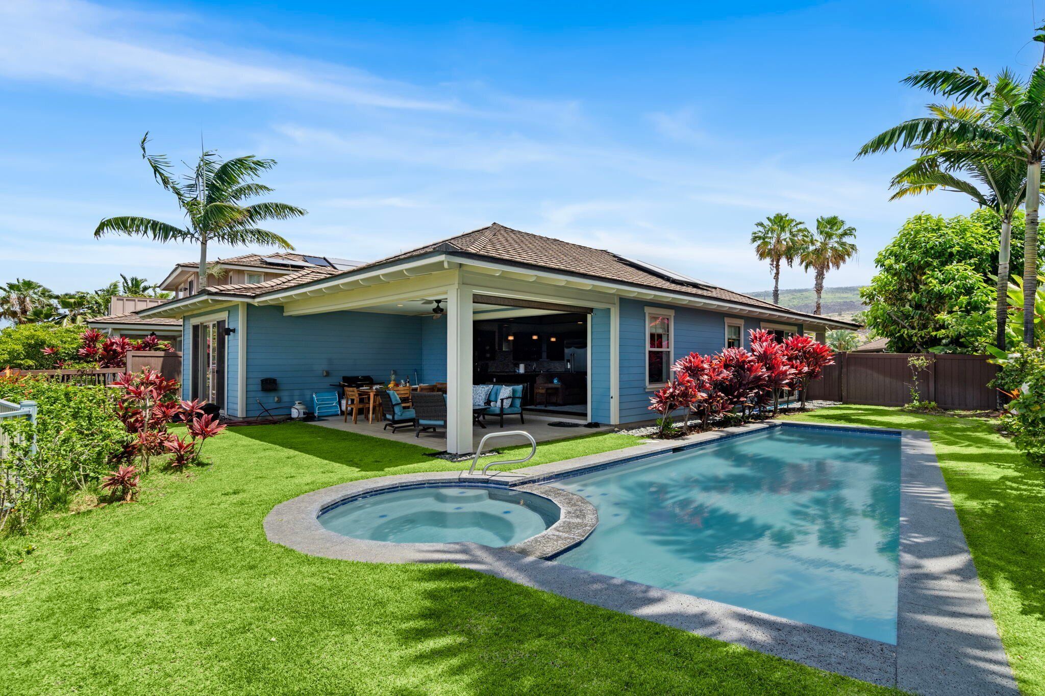 A house with a covered patio, a swimming pool, and a well-maintained lawn.