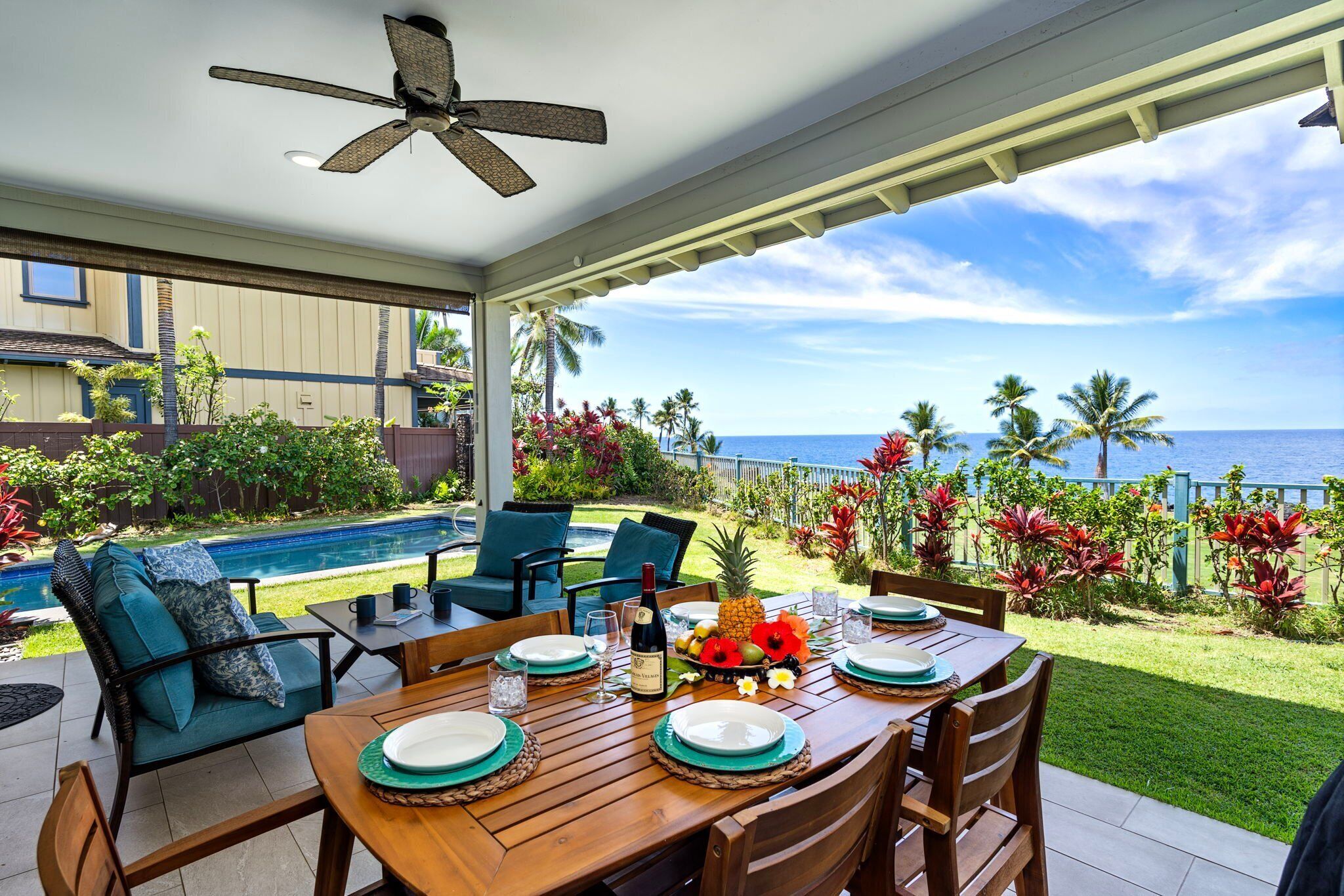 A covered patio with a wooden table set for dining, a pool, and a view of the ocean.