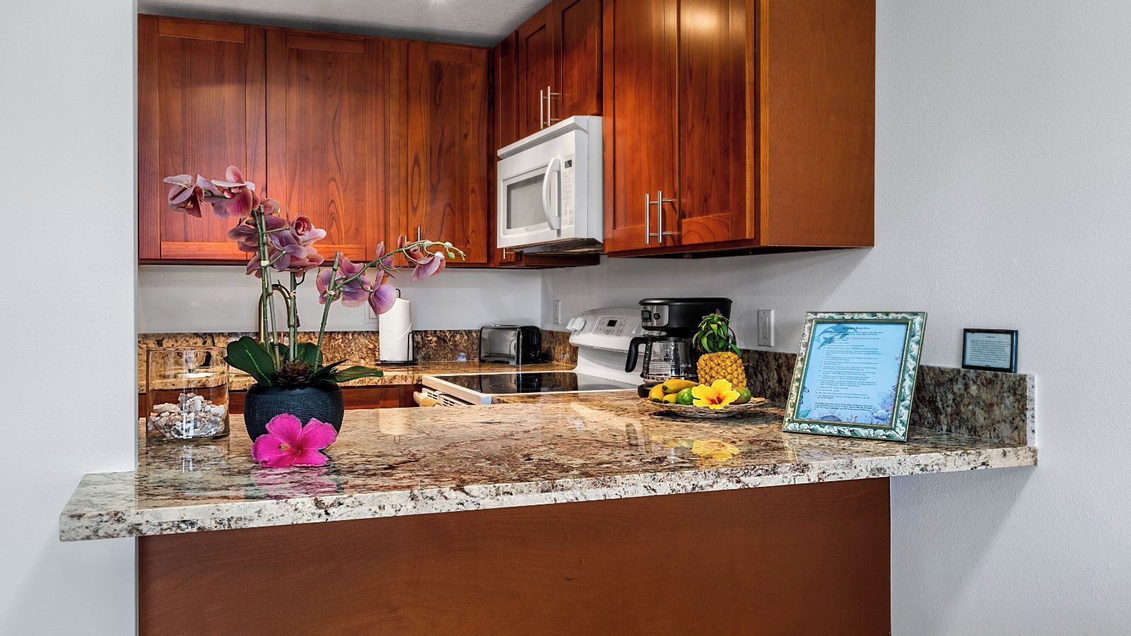 A kitchen with wooden cabinets, a microwave, a coffee maker, and a granite countertop.