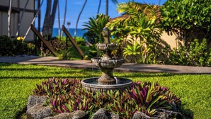 Una fuente de piedra con varios niveles en un jardín ajardinado, con césped verde y follaje púrpura.