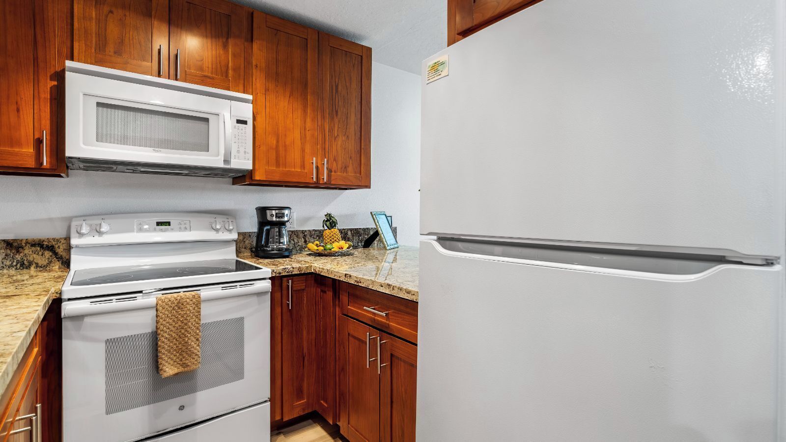 A kitchen with wooden cabinets, a white microwave, a white stove, and a white refrigerator.