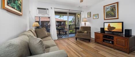 A living room with a sofa, armchair, TV, and wooden flooring.