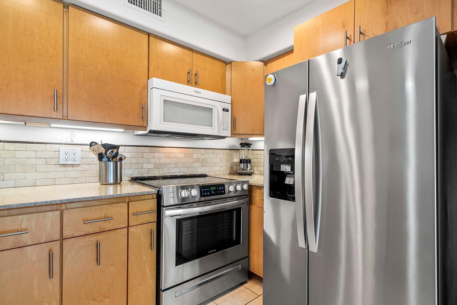 Una cocina moderna con electrodomésticos de acero inoxidable, gabinetes de madera, un microondas, un refrigerador y una cafetera.