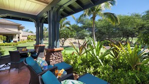 An outdoor patio with wicker furniture and a stone pillar, surrounded by lush greenery and palm trees. - Concierge Included - AC - Wifi - Mauna Lani Beach Access - Vrkcv (Kamuela)