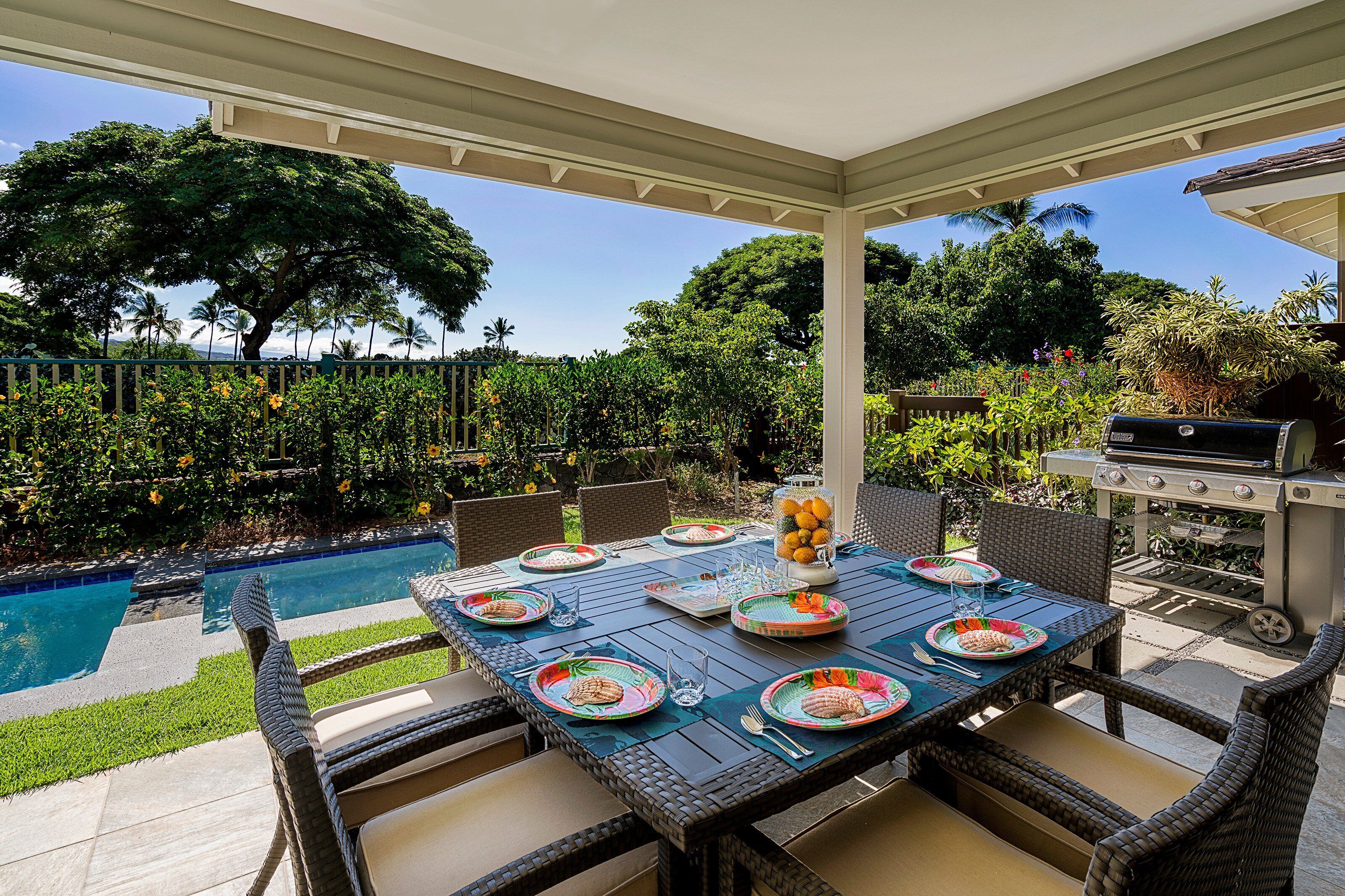 An outdoor patio with a pool, dining table set with plates and glasses, and a grill.