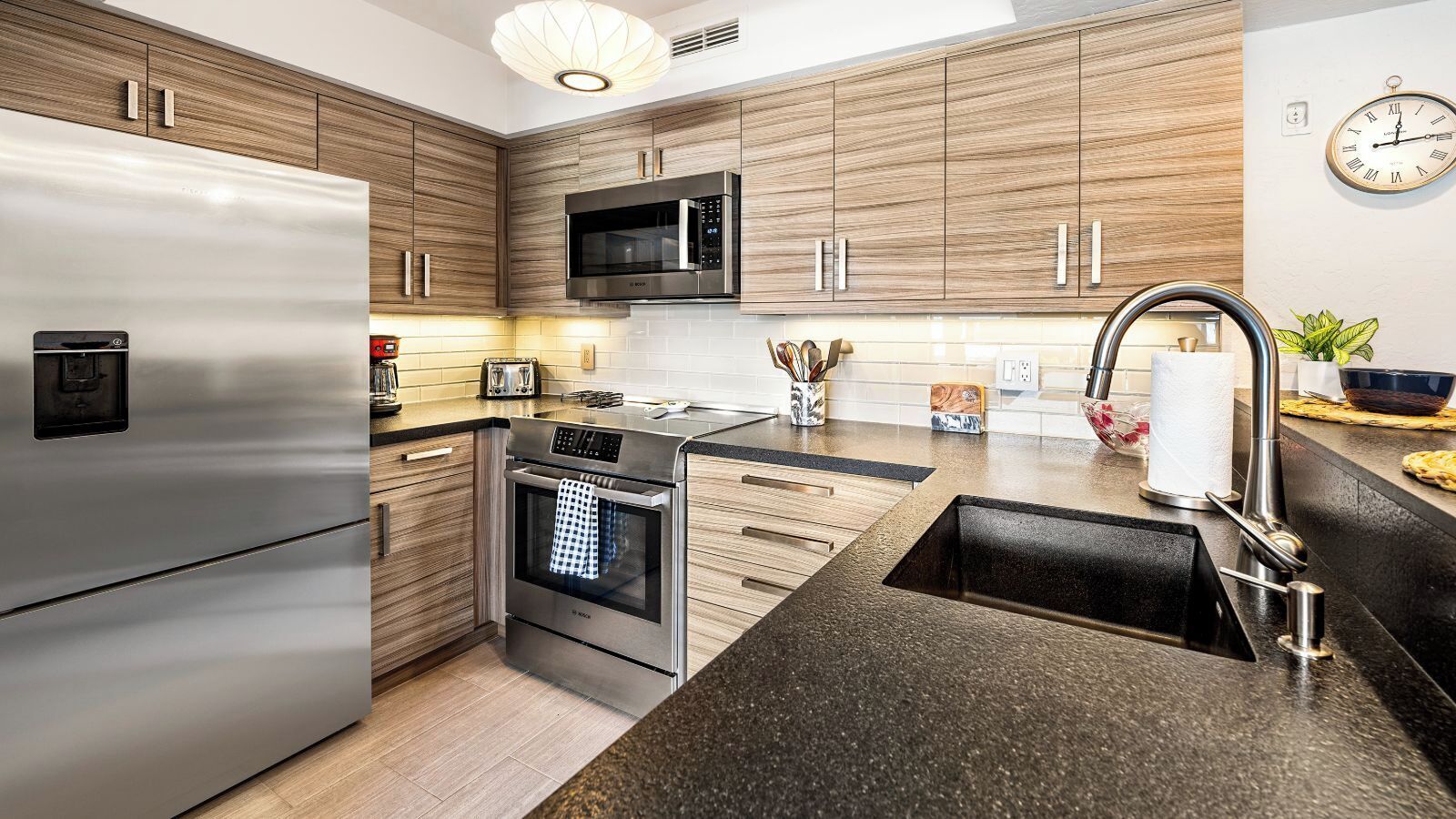 Una cocina moderna con electrodomésticos de acero inoxidable, armarios de madera y encimera negra.