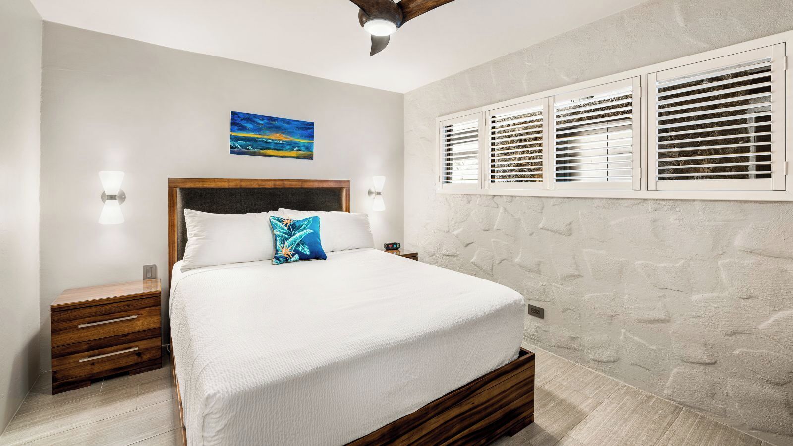 Un dormitorio con cama, mesitas de noche de madera, pared de piedra y un cuadro.