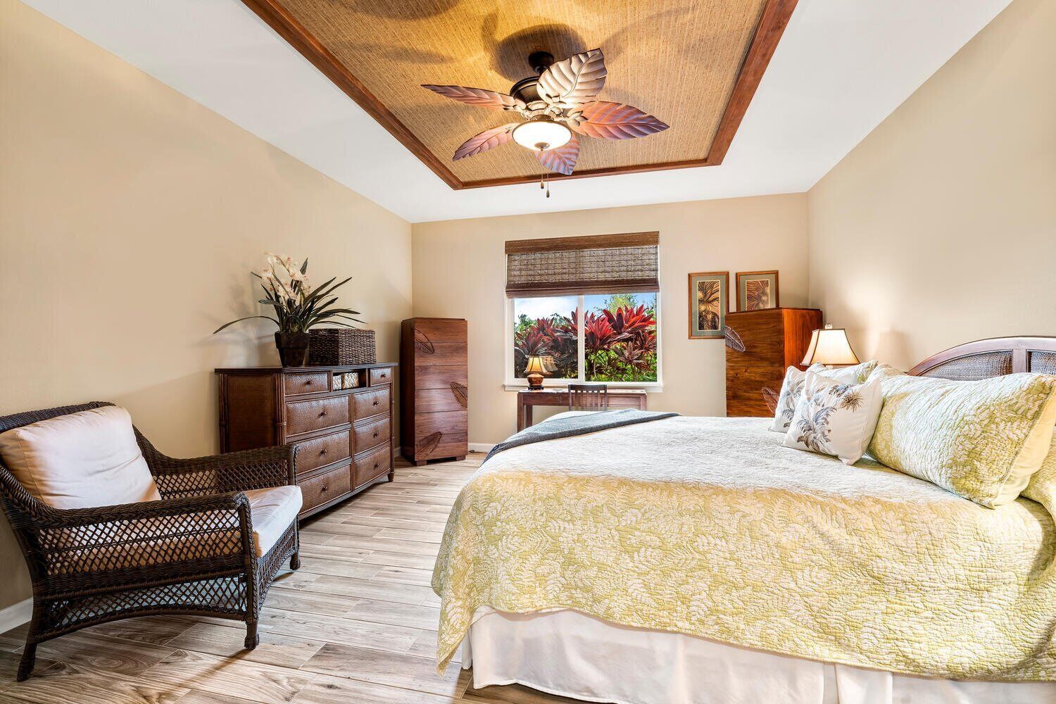A bedroom with a large bed, a wicker chair, a dresser, and a ceiling fan.