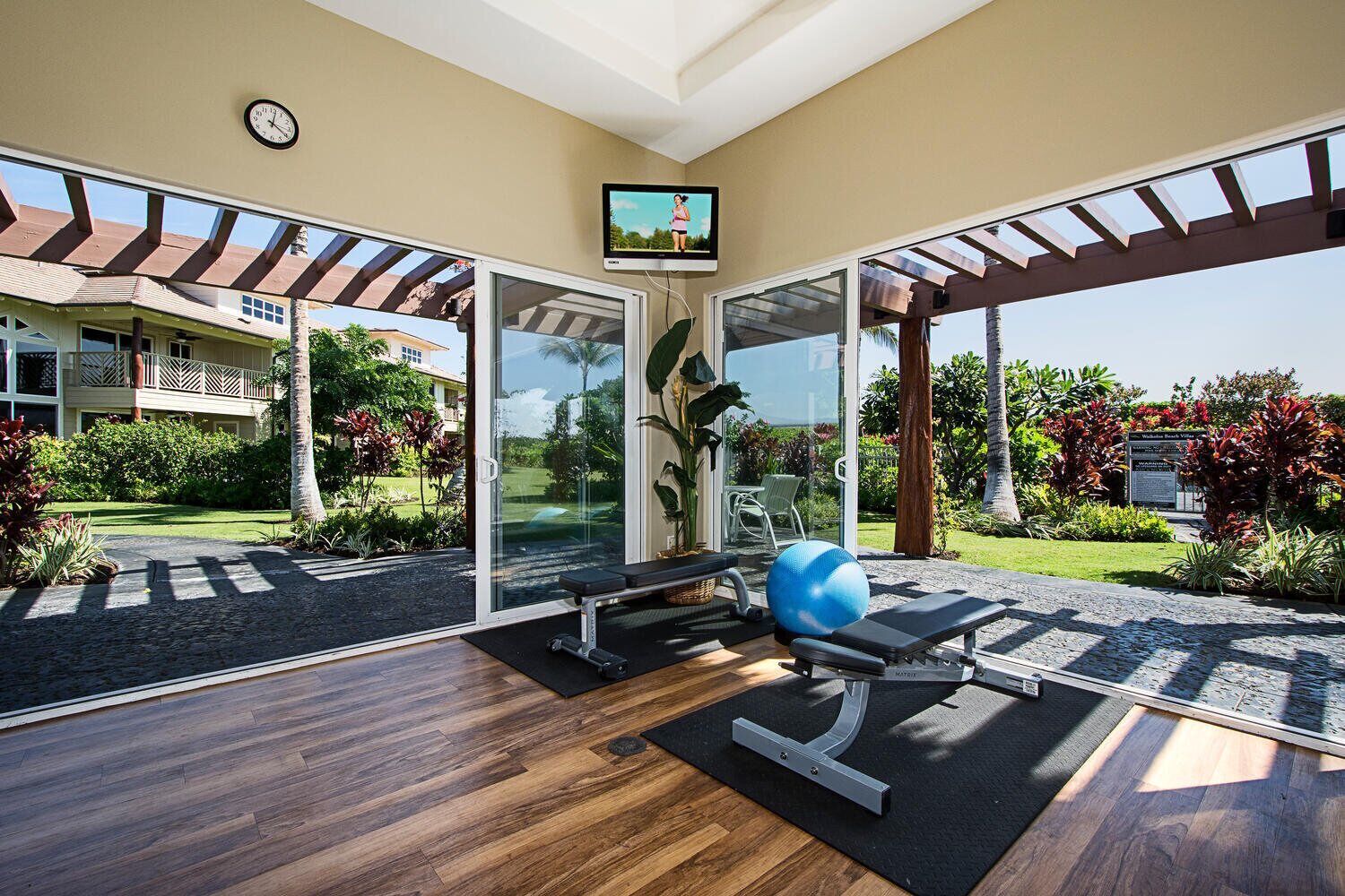 Un gimnasio con equipo de ejercicio, un ventanal y vistas a un edificio y un jardín.