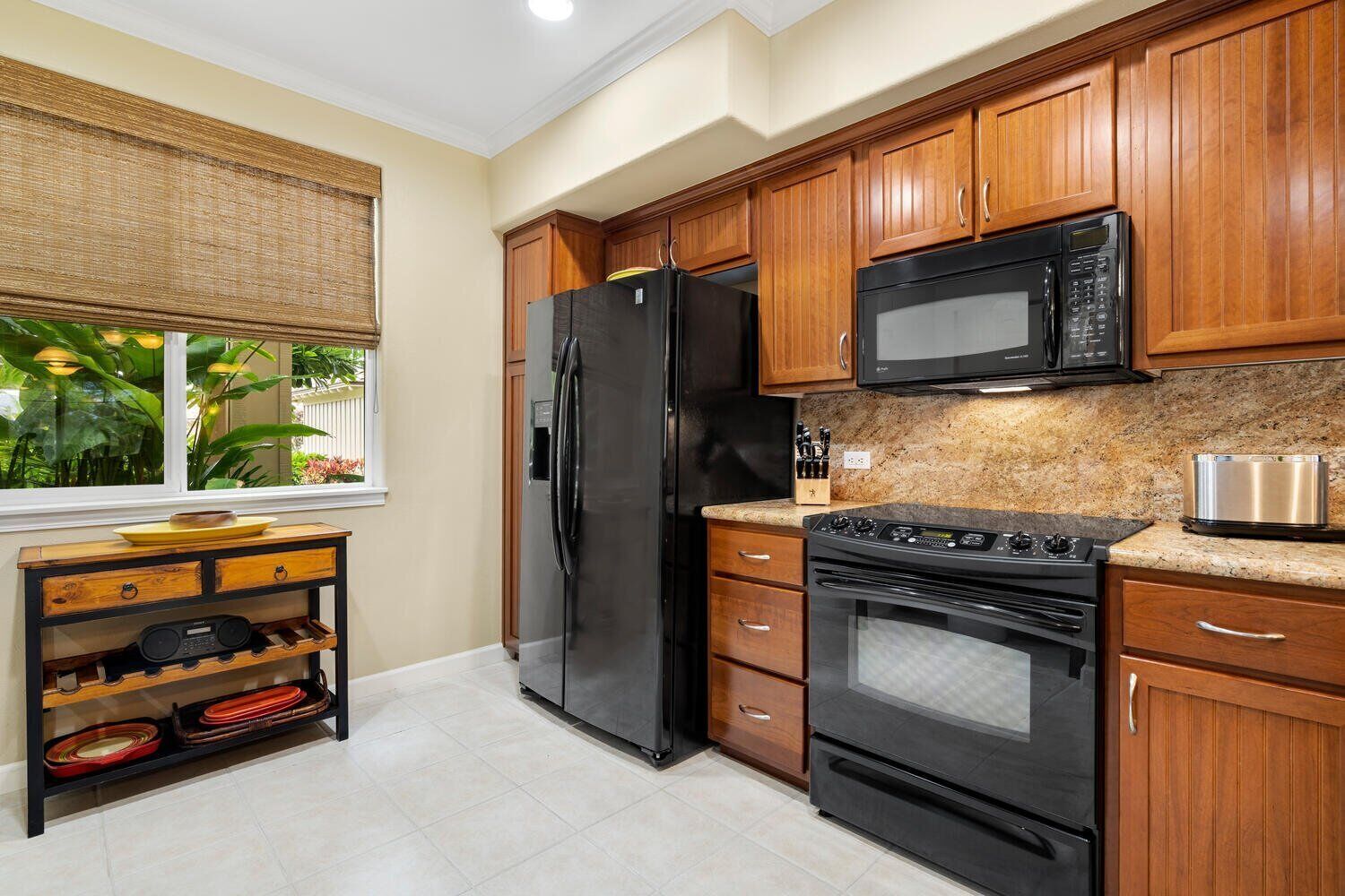 Una cocina con armarios de madera, un refrigerador negro, microondas, horno y encimera de granito.