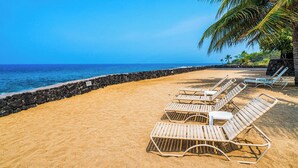 A beach with white lounge chairs and a stone wall. - Newly Remodeled - Ocean View - AC - Ground Floor - Vrkcv (Kailua-Kona)