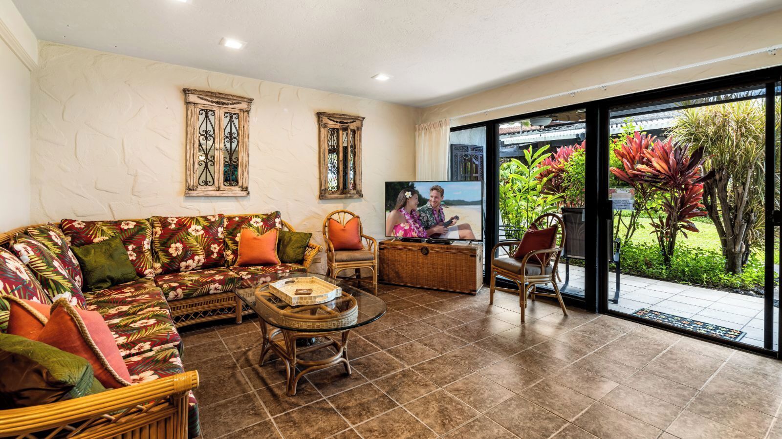 A living room with a sofa, chairs, and a coffee table. There is a television and a window with a view of greenery.