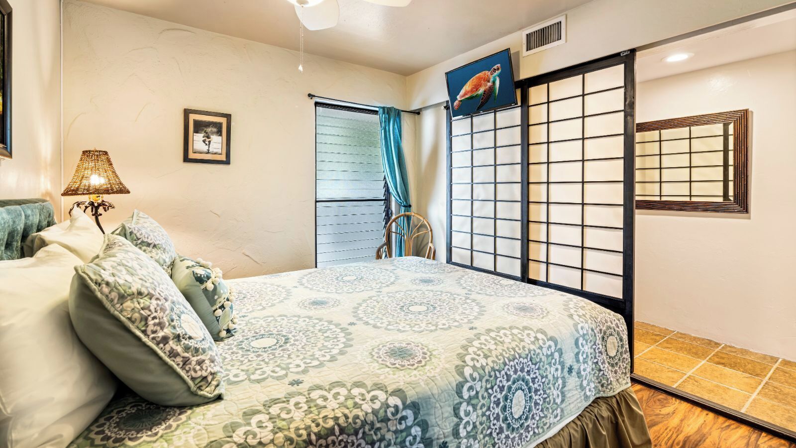 A bedroom with a bed, a chair, a TV, a window with blinds, and a decorative screen.