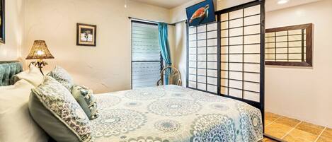 A bedroom with a bed, a chair, a TV, a window with blinds, and a decorative screen.