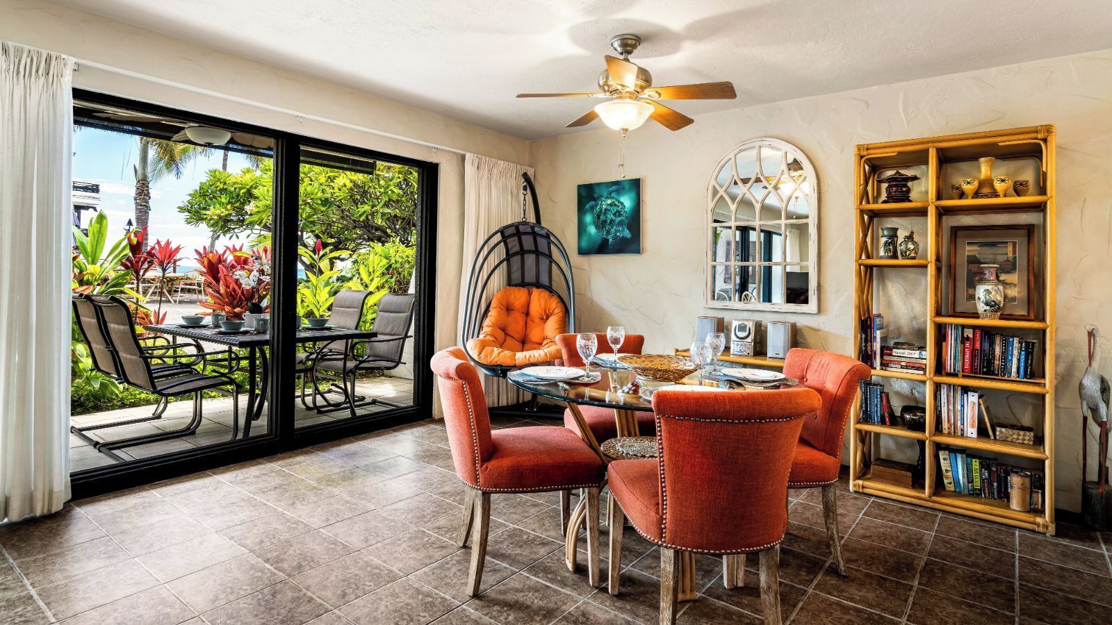 A dining area with a glass door leading to a patio, a ceiling fan, and a bookshelf filled with books and decorative items.