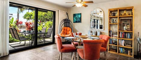 A dining area with a glass door leading to a patio, a ceiling fan, and a bookshelf filled with books and decorative items.